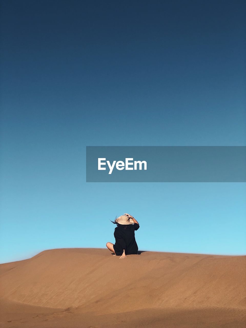 Rear view of woman siting at desert against clear blue sky