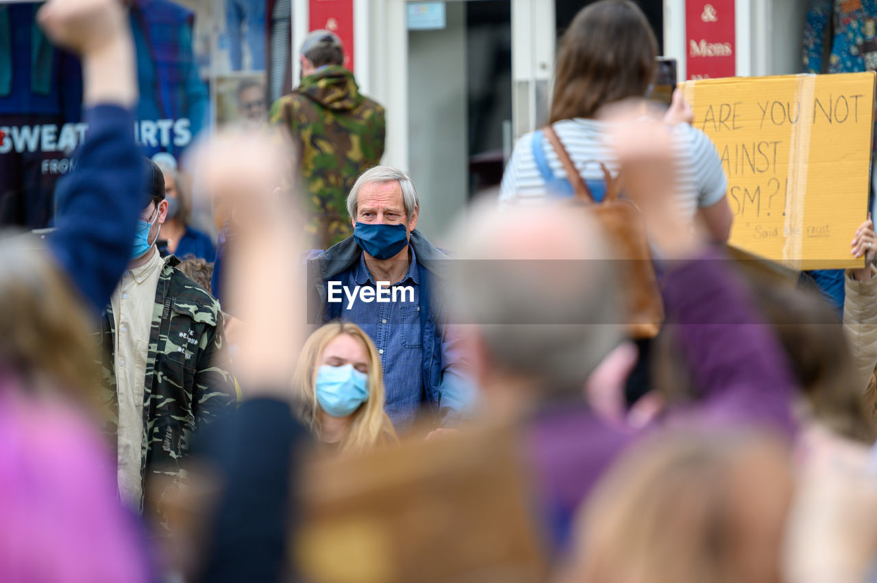 REAR VIEW OF PEOPLE STANDING AGAINST BLURRED BACKGROUND