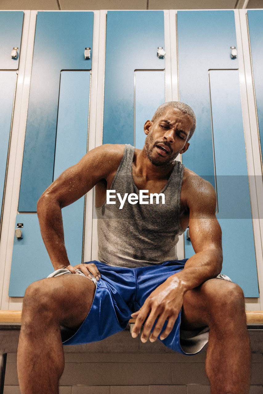 Tired male athlete taking rest while sitting in locker room