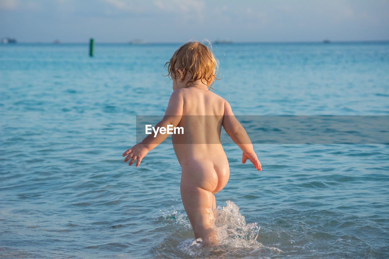 Rear view of nude toddler boy on sea shore