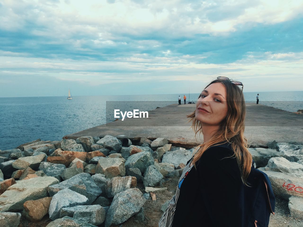 Portrait of smiling woman standing on groyne amidst sea against cloudy sky