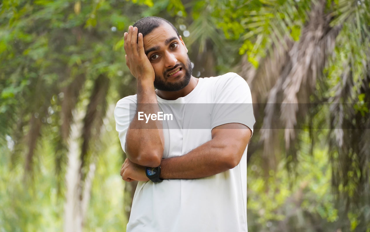 young man looking away while standing against tree trunk in forest