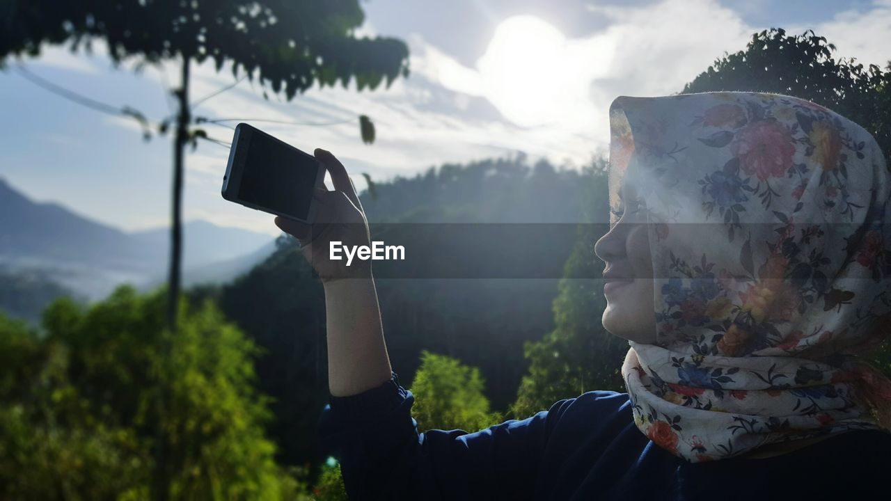 Woman wearing headscarf photographing against mountain