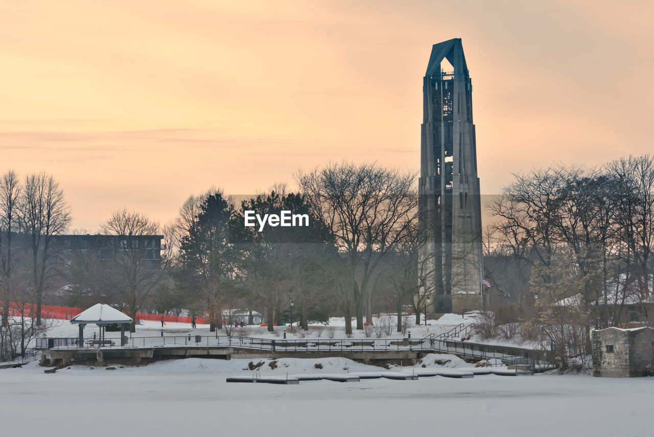 SNOW COVERED TREES AND BUILDING AGAINST SKY DURING SUNSET