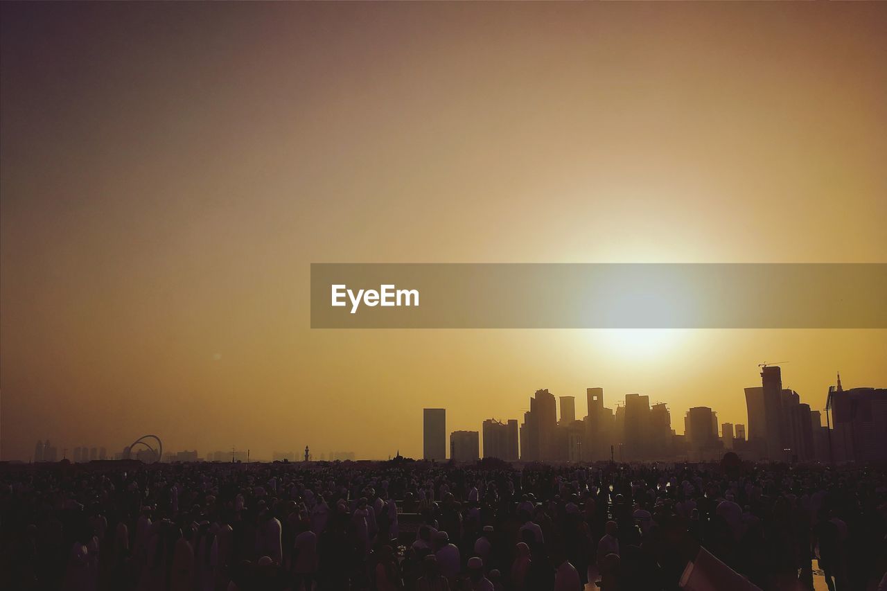 Group of people in city against sky during sunset