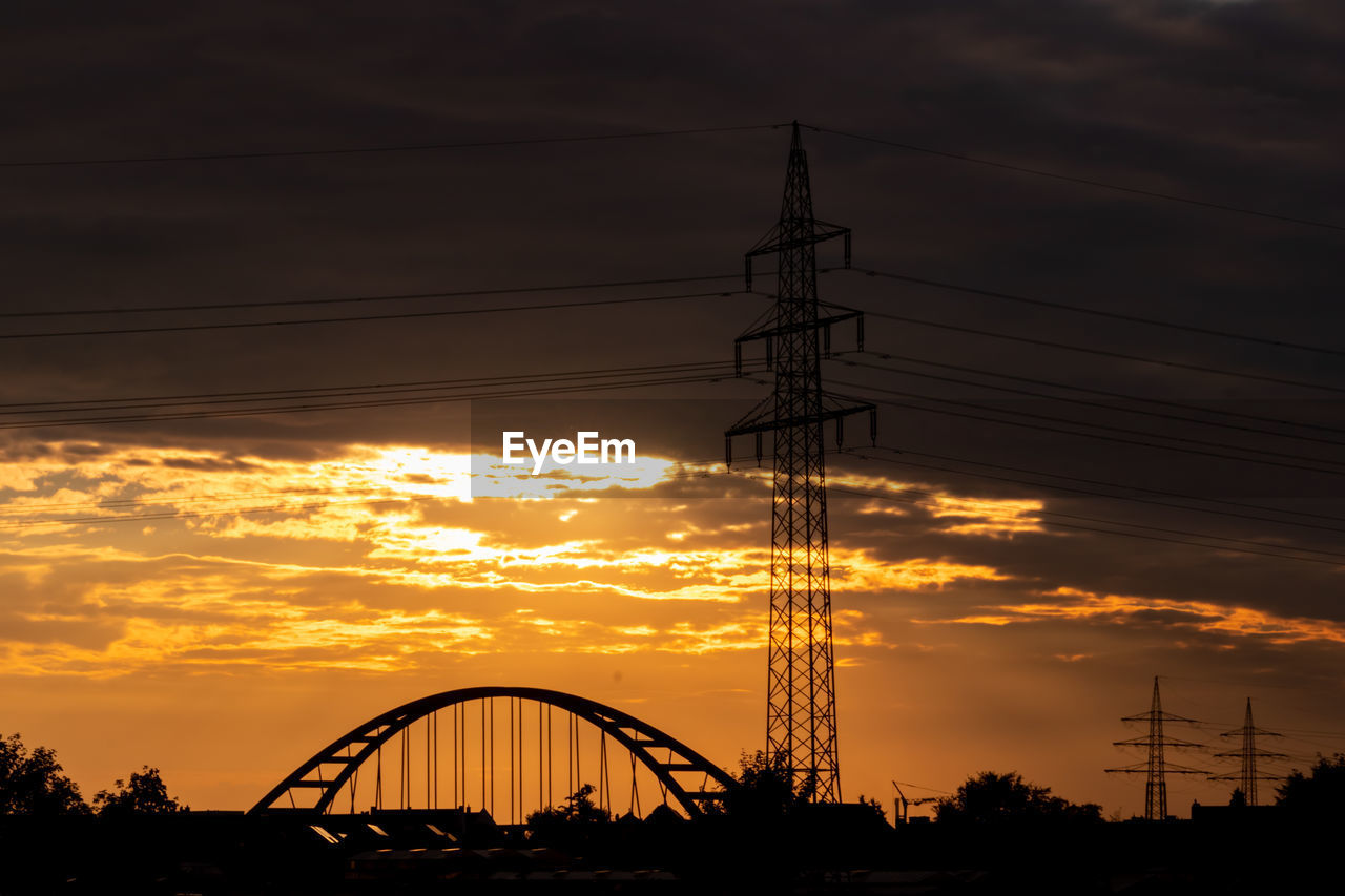 Electricity tower pylon silhouette in golden sunset and orange sky for sustainable energy renewable