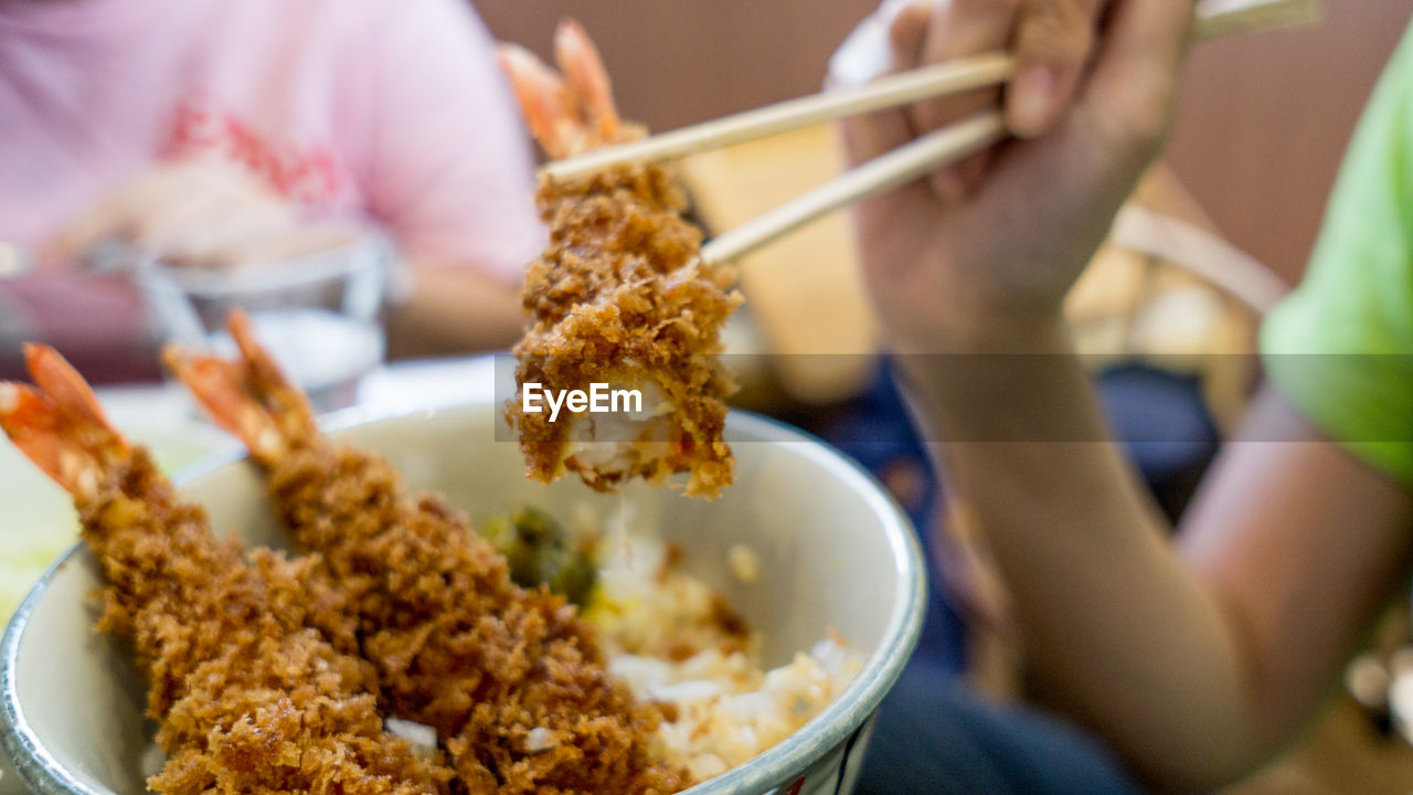 Cropped hand of person holding katsu with chopsticks over bowl