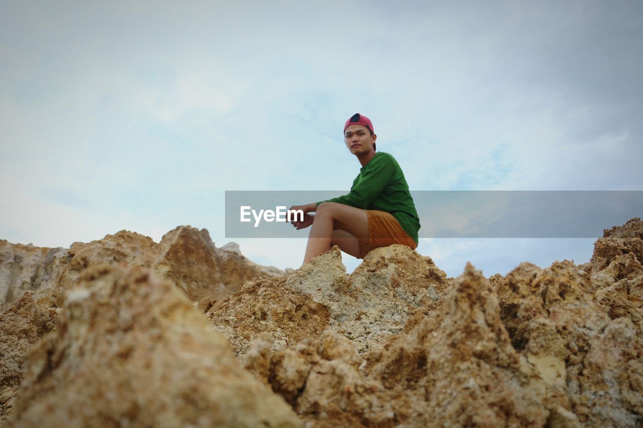 Low angle view of man sitting on rock formation against sky