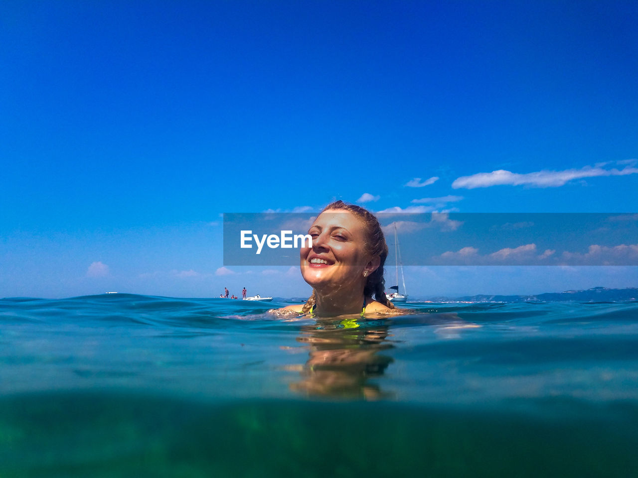 Portrait of smiling young woman swimming in sea against blue sky