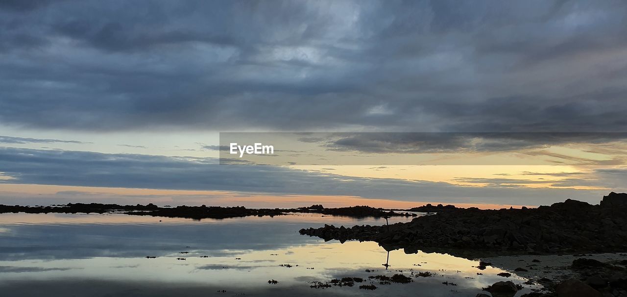 SCENIC VIEW OF LAKE AGAINST DRAMATIC SKY AT SUNSET