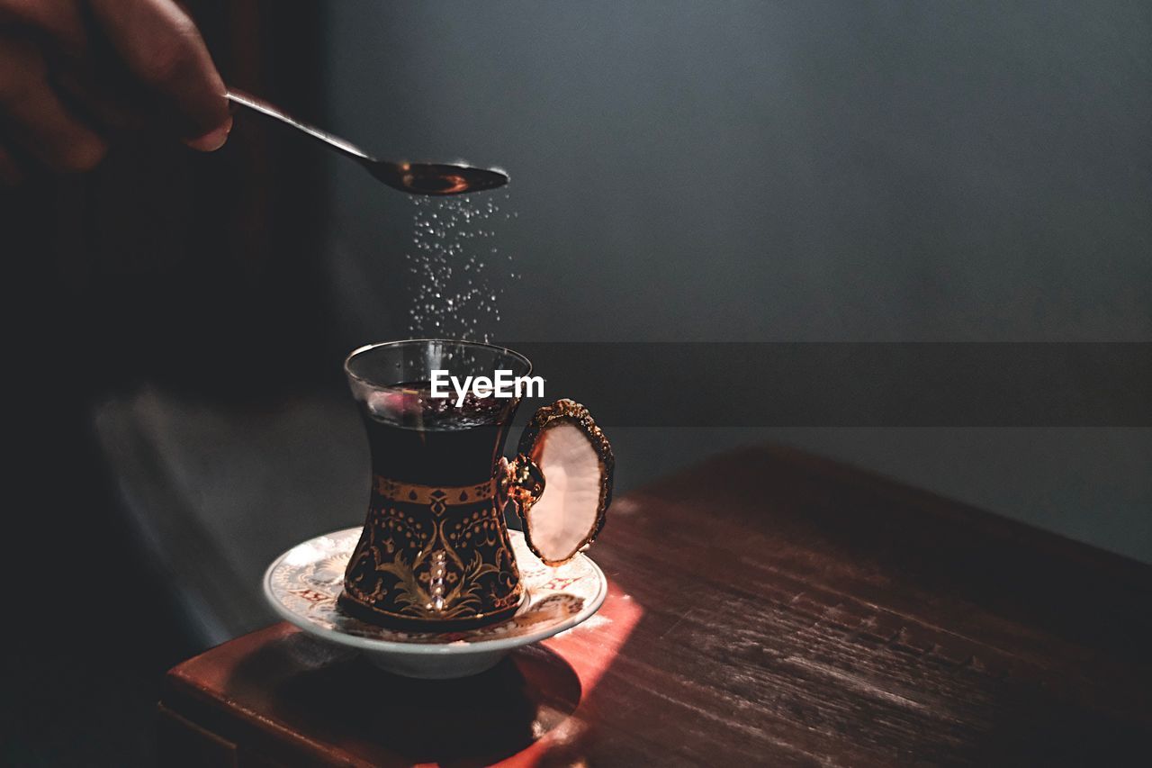 Close-up of hand pouring sugar in drink on table