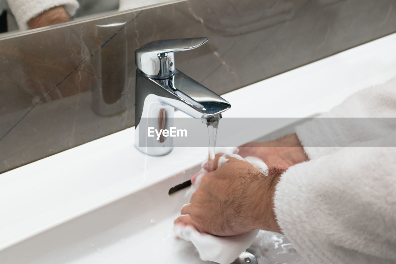 Cropped image of man washing hands in bathroom