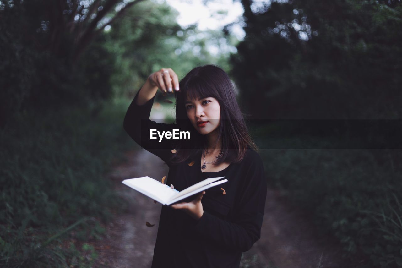 Woman holding book while standing in forest