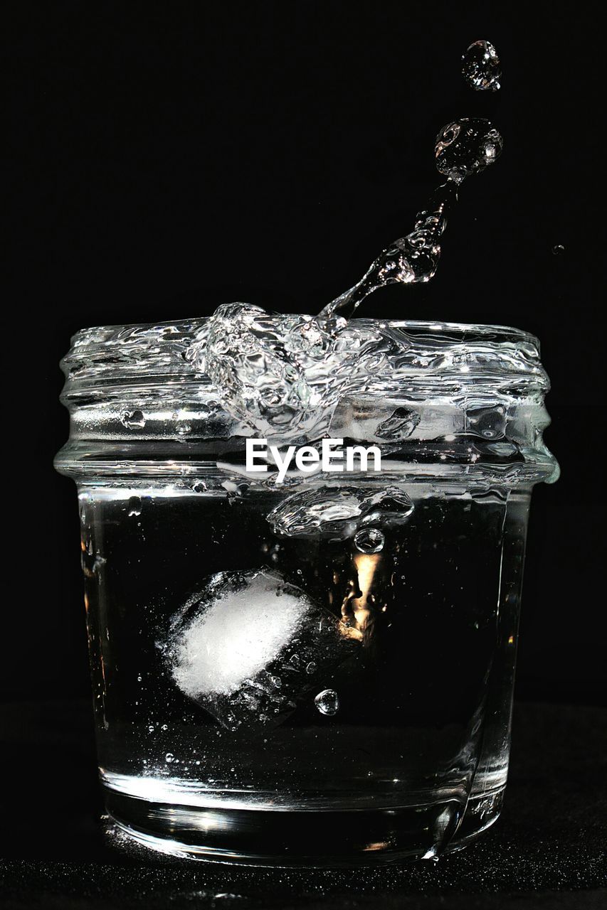 Close-up of drink splashing in glass with ice against black background