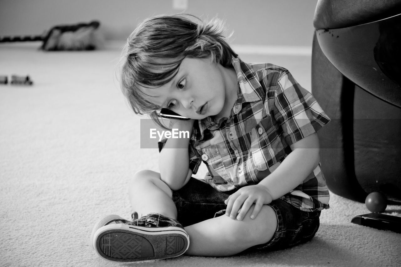 Little boy holding mobile phone to ear while sitting on floor