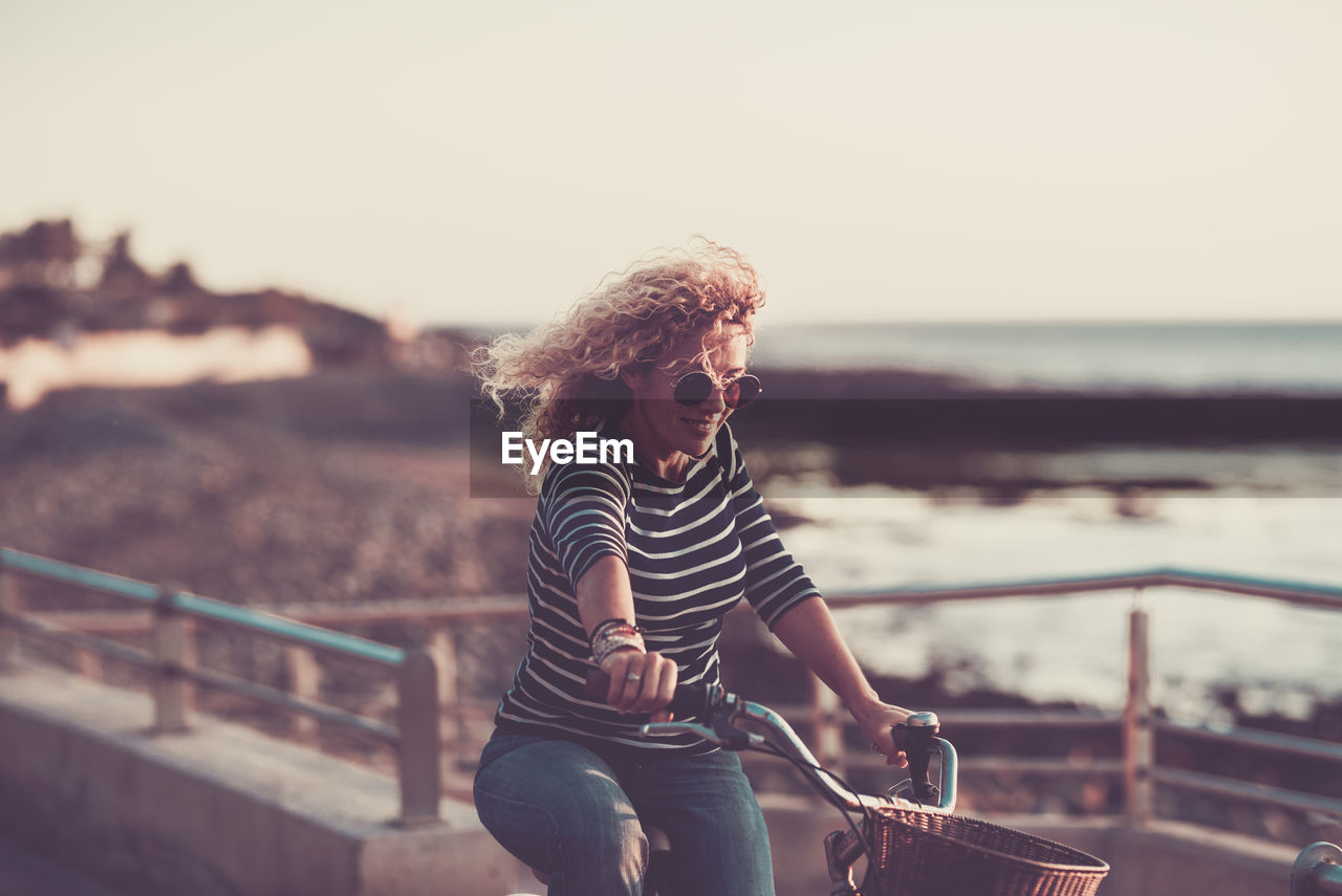 WOMAN STANDING BY RAILING AGAINST SEA