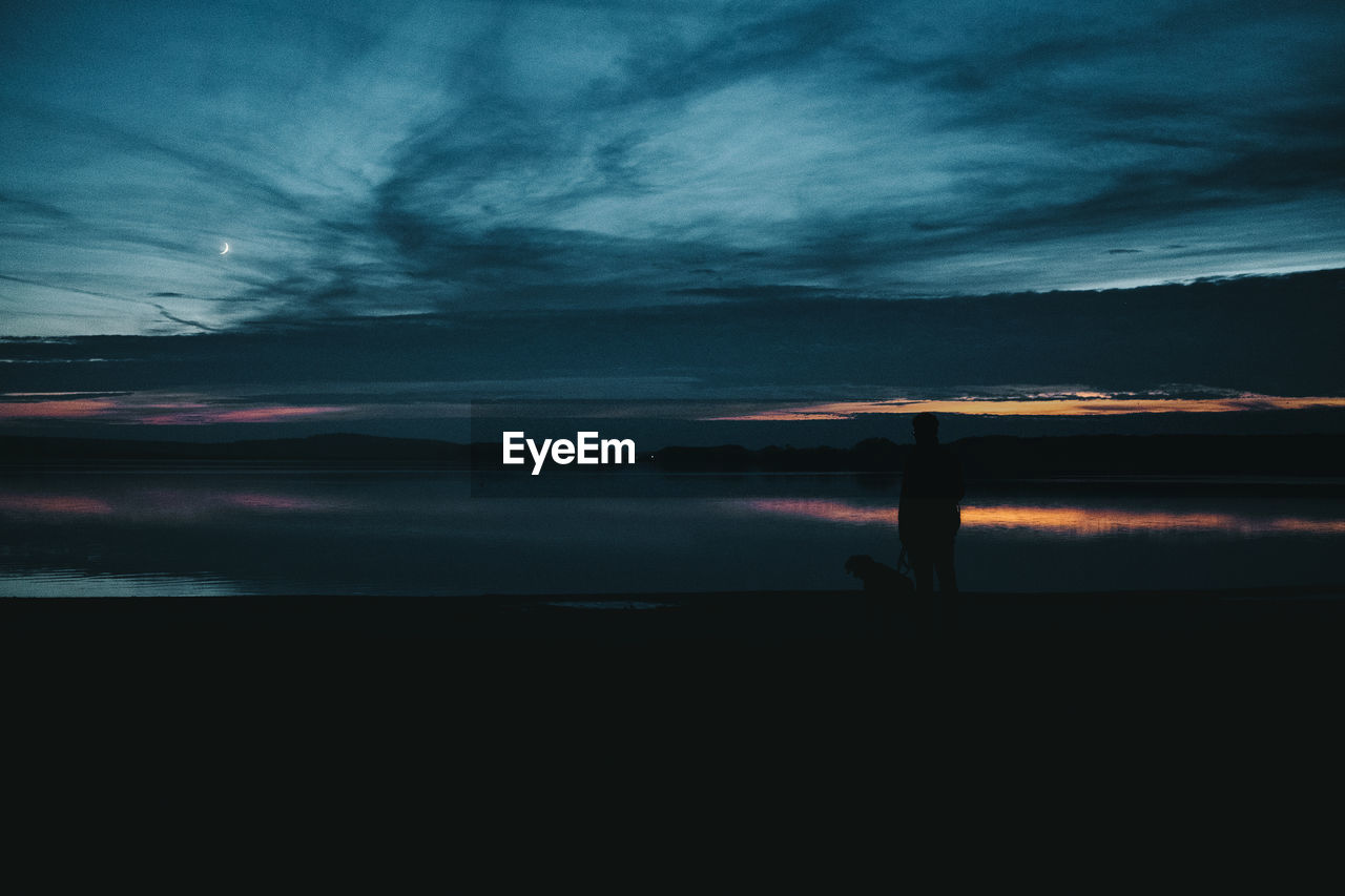 Silhouette man with dog standing by lake during sunset