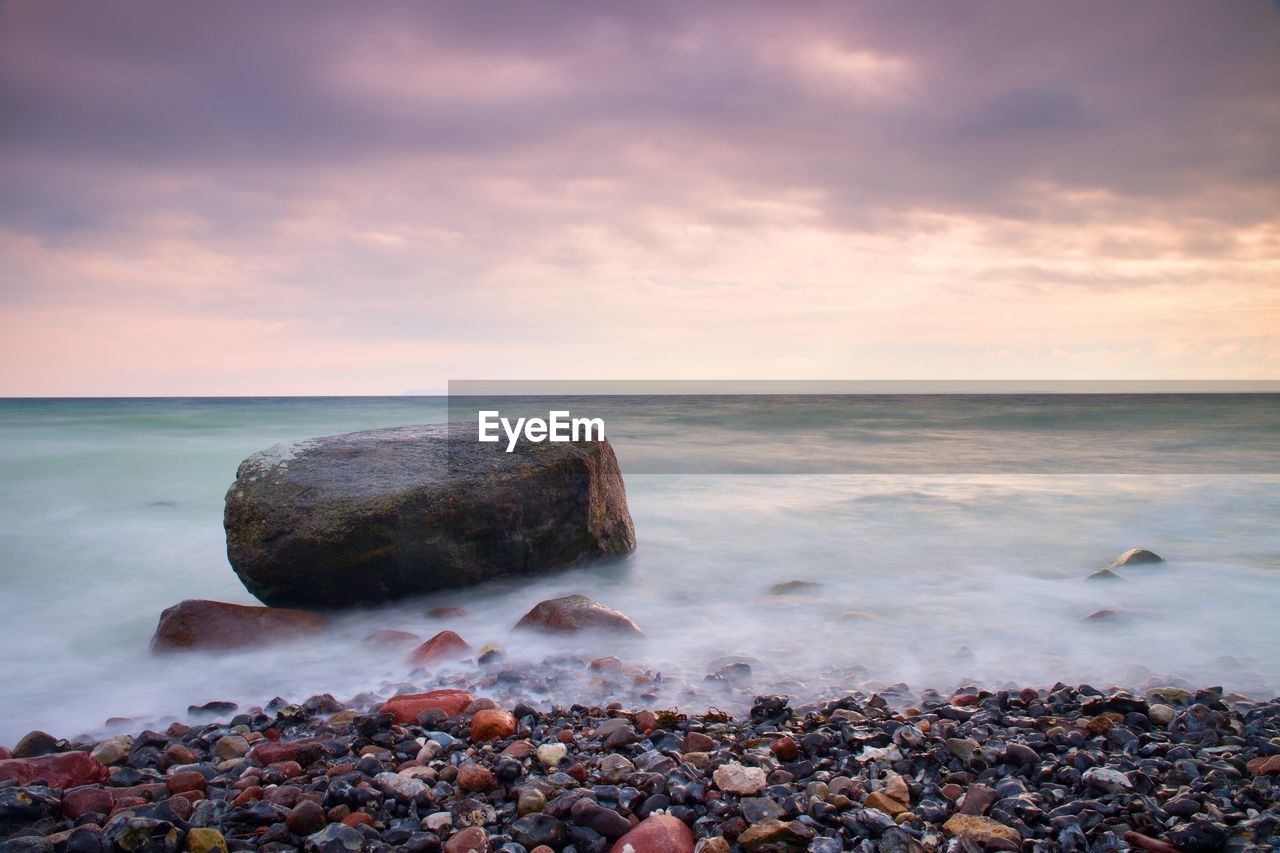  big boulders sticking out from smooth wavy sea. pink horizon with first hot sun style toned effect