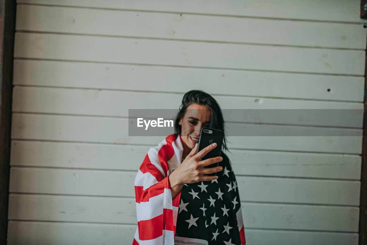 Woman wearing american flag using phone against wall