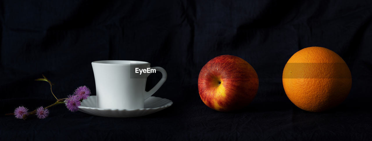 CLOSE-UP OF APPLE AND COFFEE ON TABLE AGAINST BLACK BACKGROUND