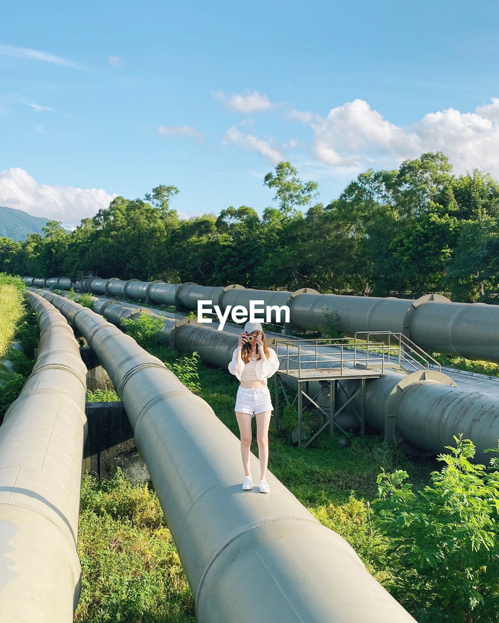 Full length of woman photographing while standing on pipes