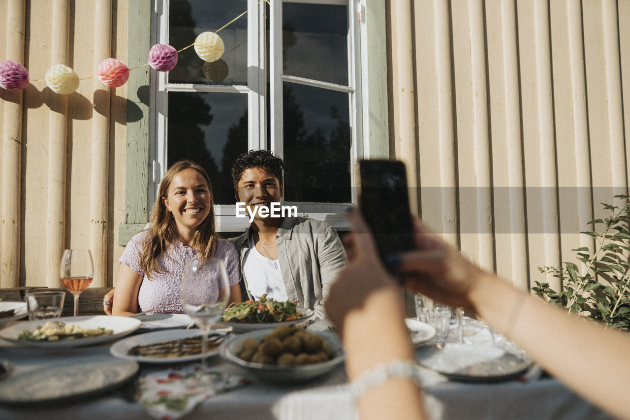 Hand of woman clicking picture of male and female friends during dinner party at cafe