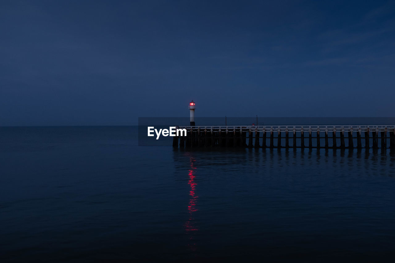 Lighthouse on pier by sea against sky