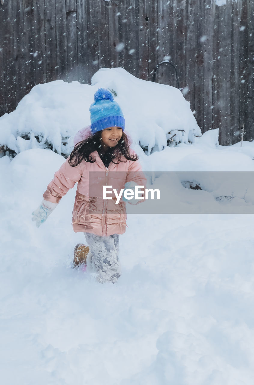 Diverse mixed race pre school toddler girl outdoors in winter playing with snow 