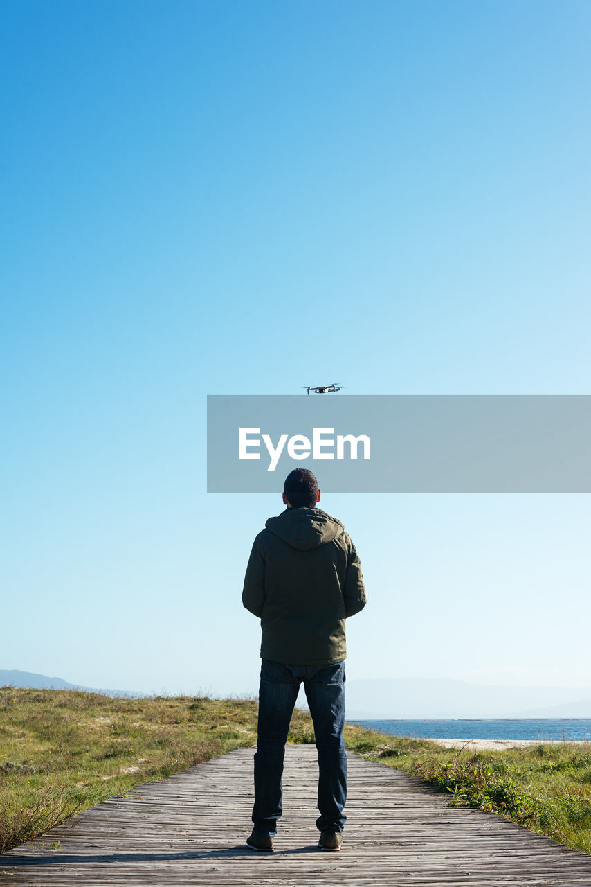 Young man flying a dron near to the beach backwards