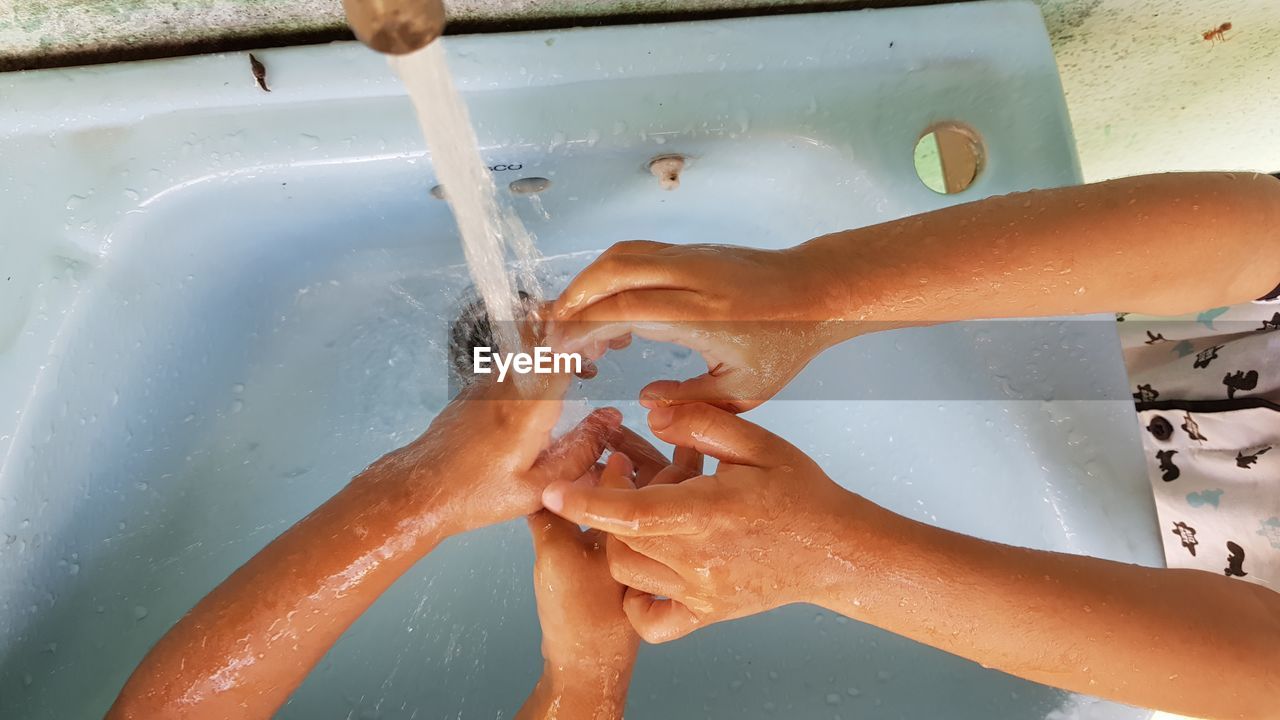 HIGH ANGLE VIEW OF HANDS HOLDING WATER IN CONTAINER