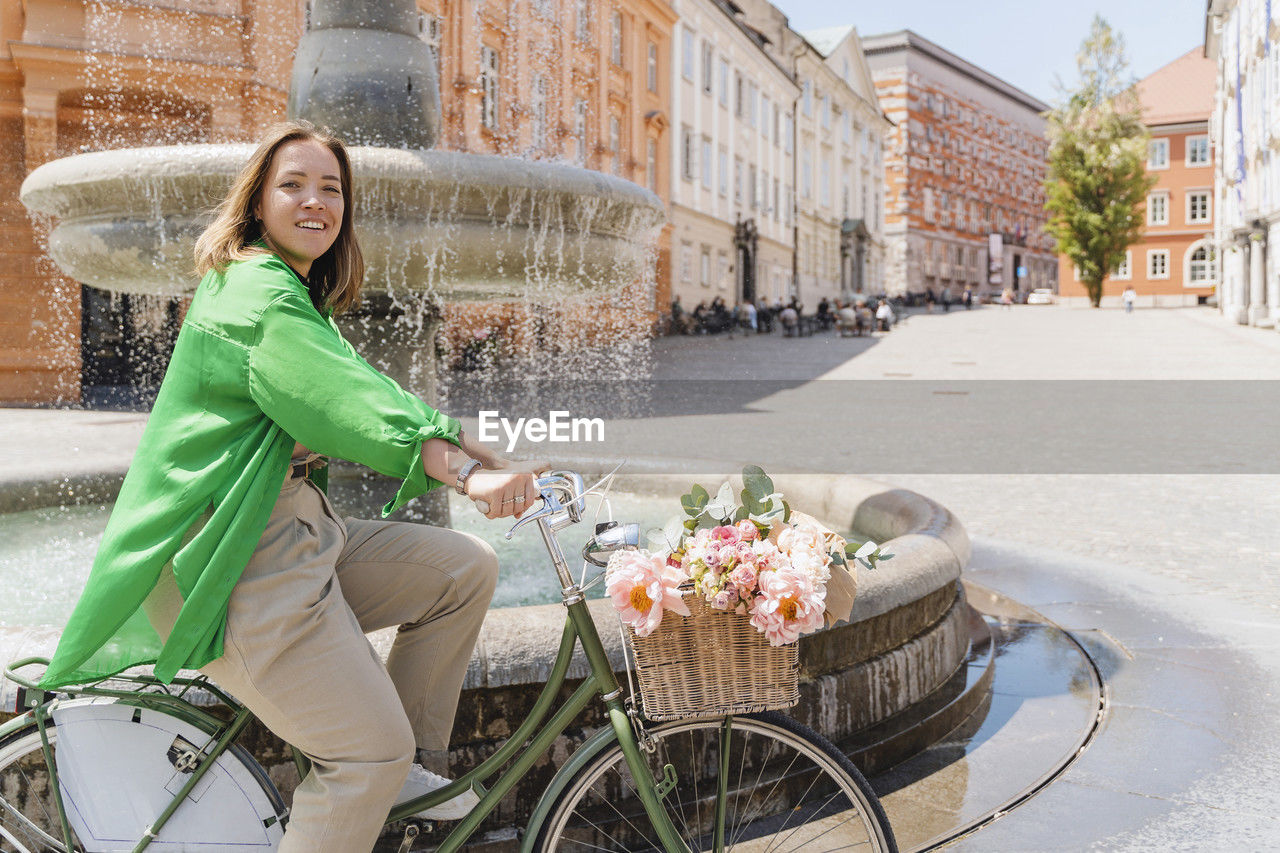 Smiling woman riding bicycle by fountain in city