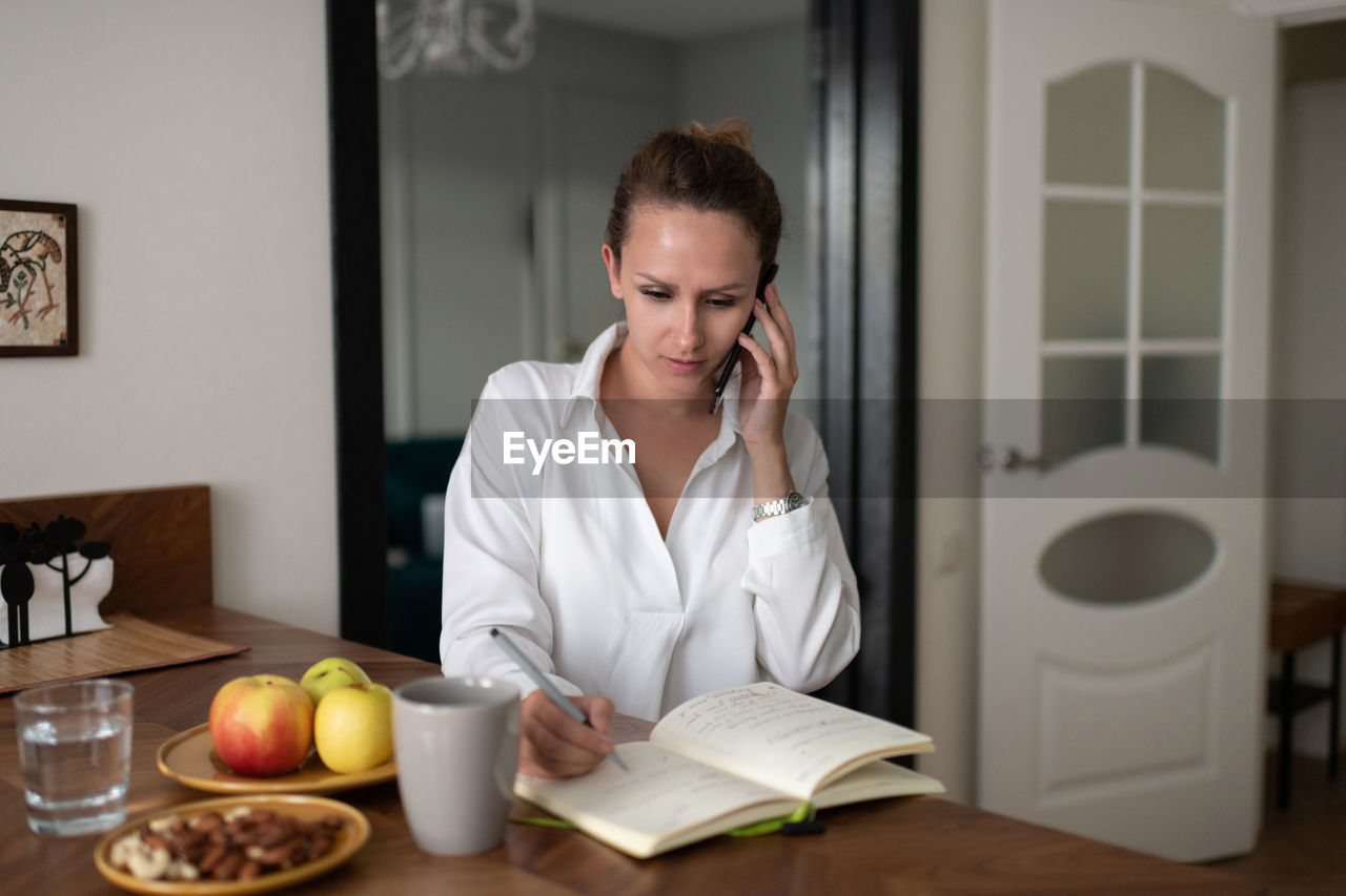 Businesswoman speaking on smartphone and making notes