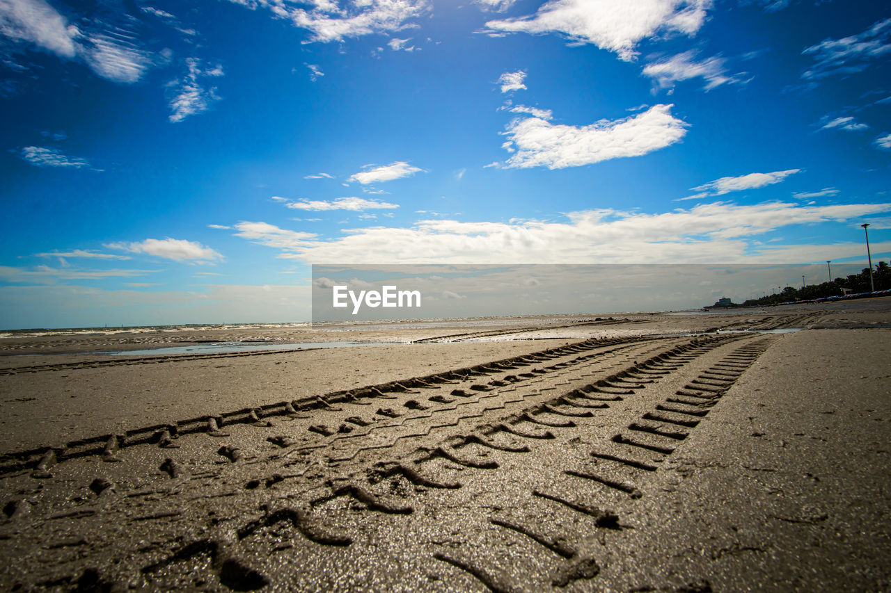 SURFACE LEVEL OF TIRE TRACKS ON BEACH AGAINST SKY