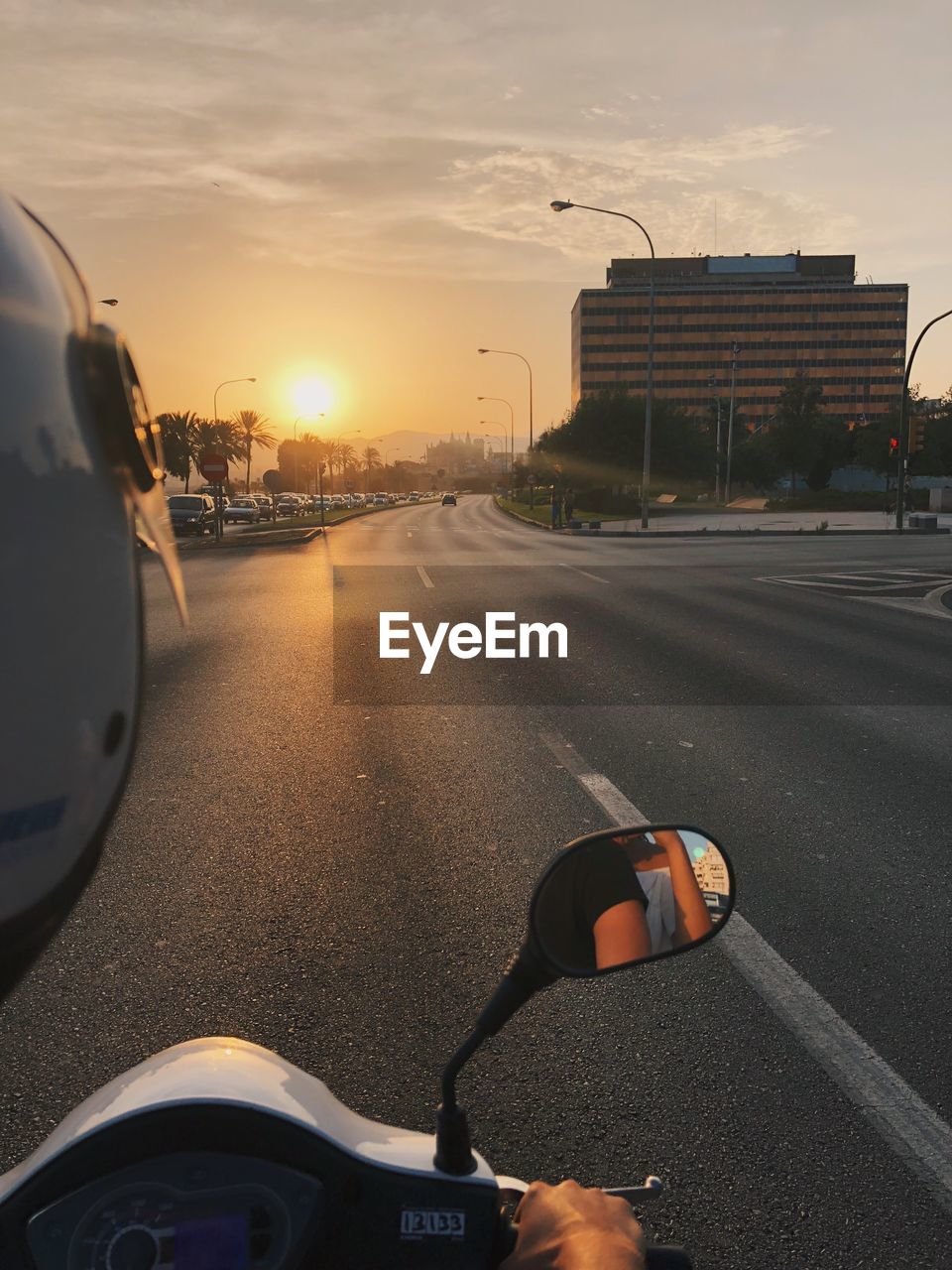 Close-up of man riding motor scooter on street against sky during sunset