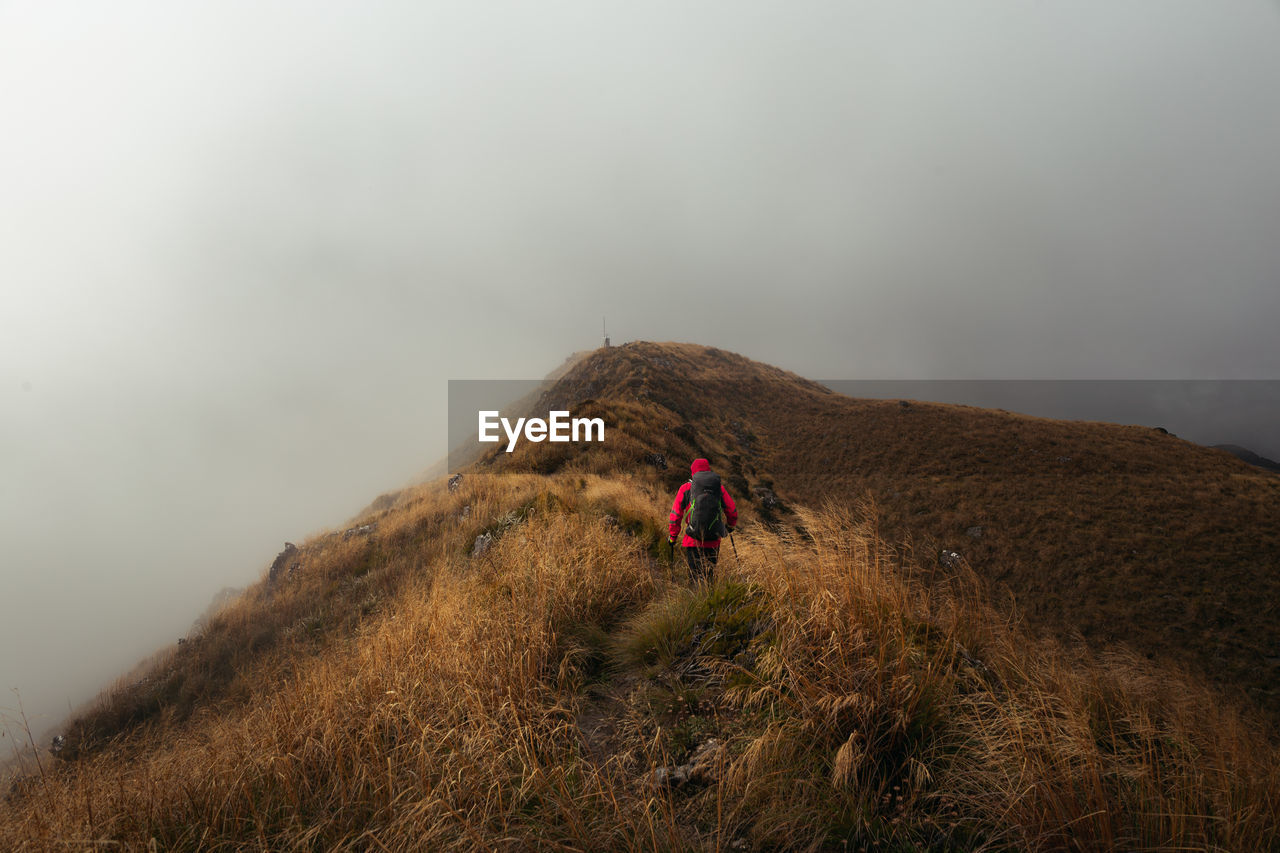 MAN CLIMBING ON MOUNTAIN AGAINST SKY DURING FOGGY WEATHER