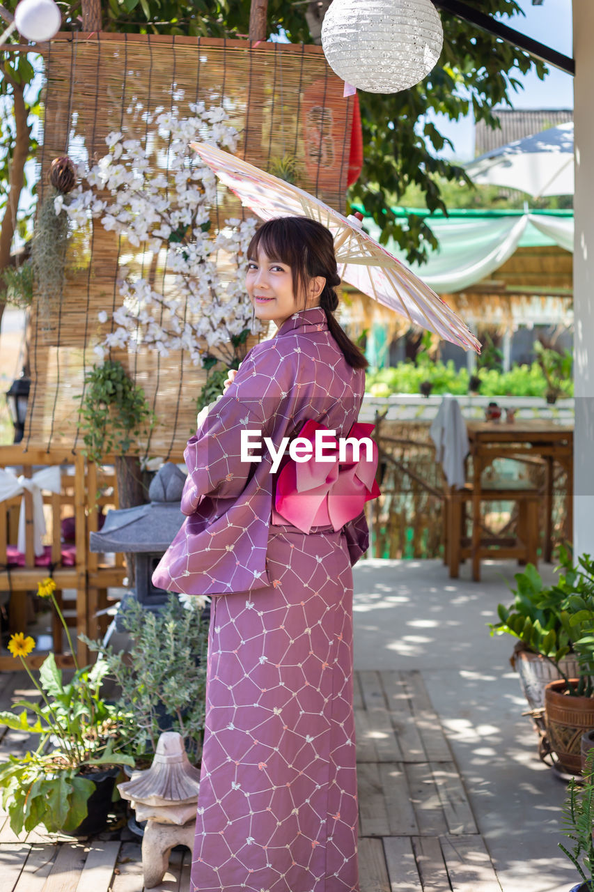 Portrait of woman standing by flowering plants outdoors