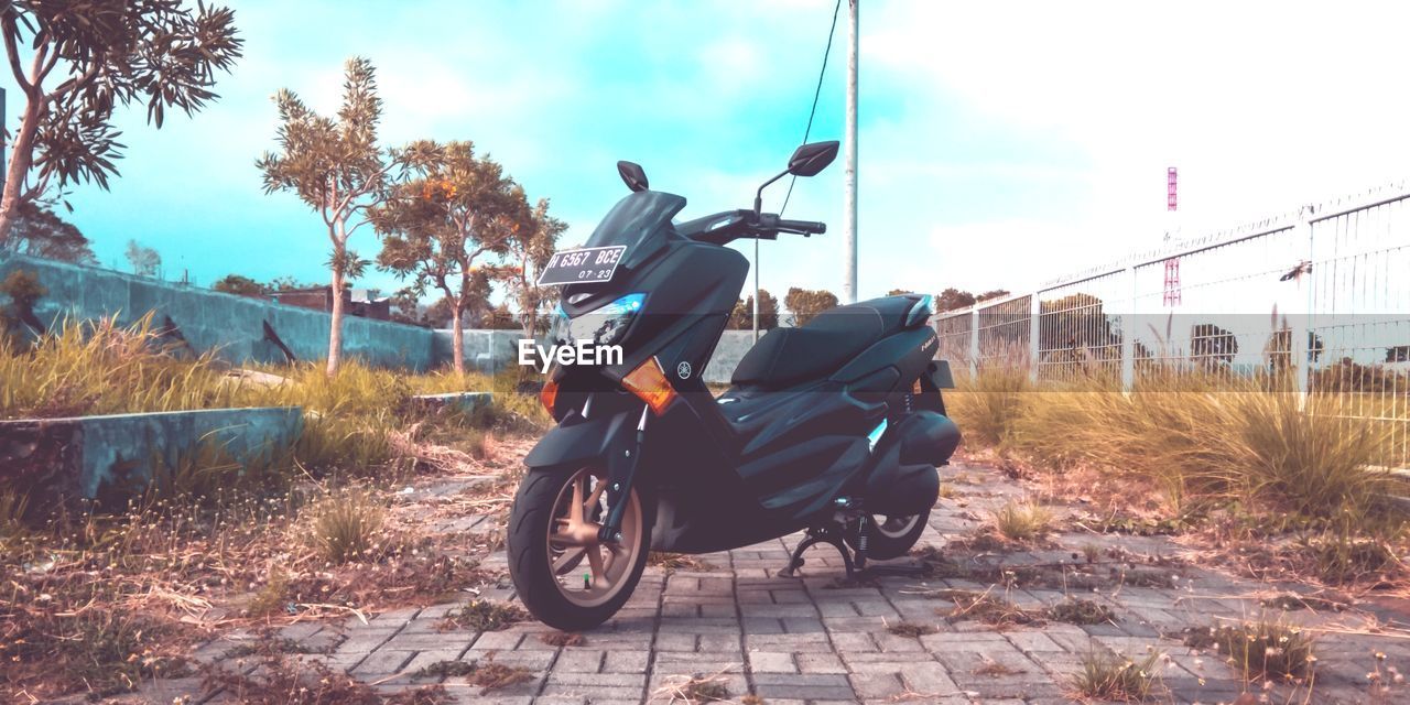 MAN RIDING MOTOR SCOOTER ON ROAD BY FIELD