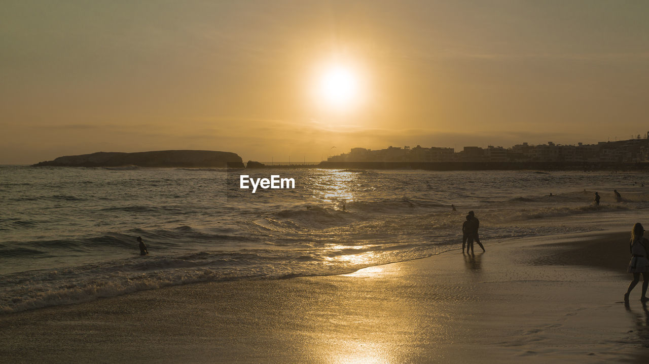 water, sky, sea, sunset, beach, land, beauty in nature, nature, ocean, sunlight, horizon, sun, wave, shore, body of water, scenics - nature, silhouette, coast, men, tranquility, reflection, dawn, lifestyles, leisure activity, tranquil scene, two people, sand, adult, idyllic, motion, evening, vacation, holiday, outdoors, trip, wind wave, walking, sports, horizon over water, orange color, full length, togetherness, women, lens flare, sunbeam