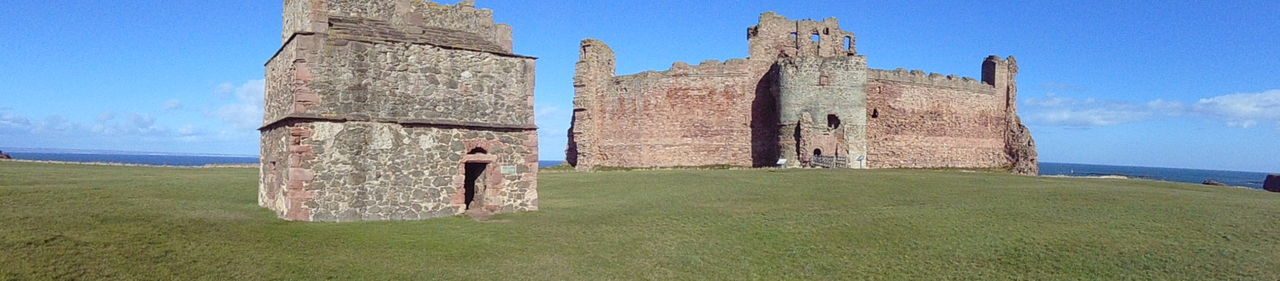 OLD RUINS ON GRASSY FIELD AGAINST BLUE SKY