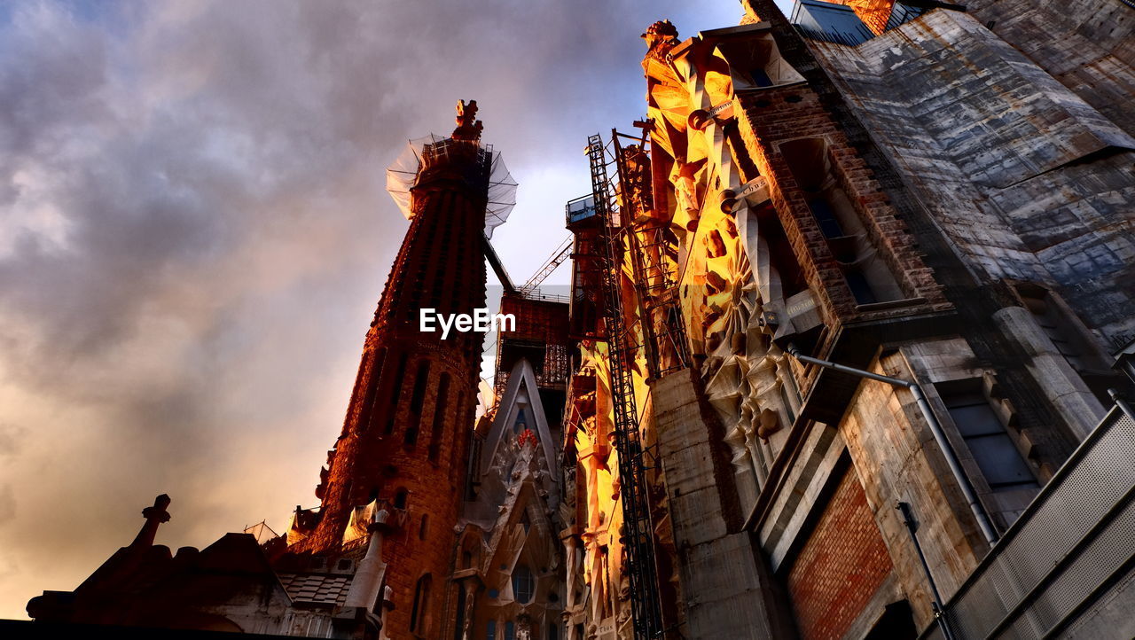 Low angle view of sagrada familia against cloudy sky during sunset