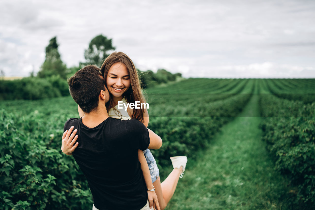 Smiling young woman and man standing on field against sky