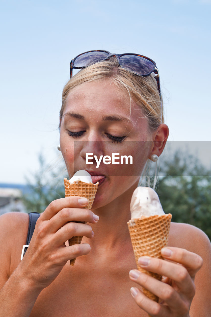 Woman licking ice cream against sky