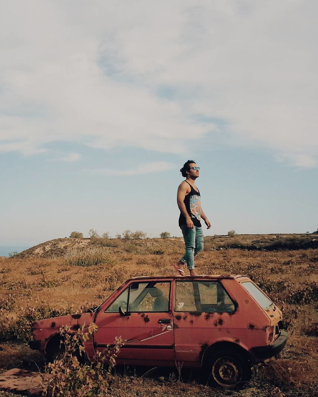 Full length of man standing on abandoned car roof over field against sky