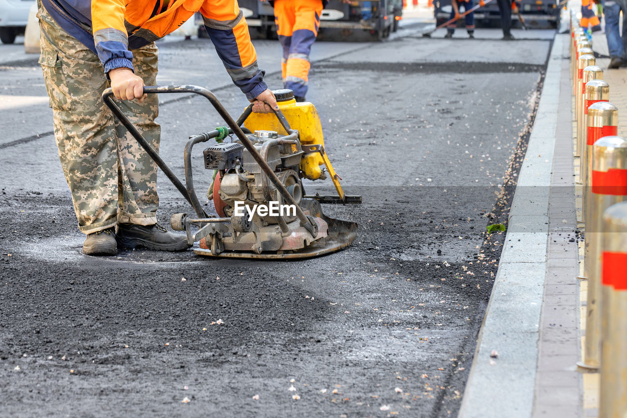 asphalt, transportation, road, street, city, road construction, occupation, working, construction industry, mode of transportation, men, day, construction site, manual worker, firefighter, vehicle, sign, protection, bicycle, industry, construction worker, city street, outdoors, adult, reflective clothing, low section, clothing, land vehicle, traffic cone, group of people, cone