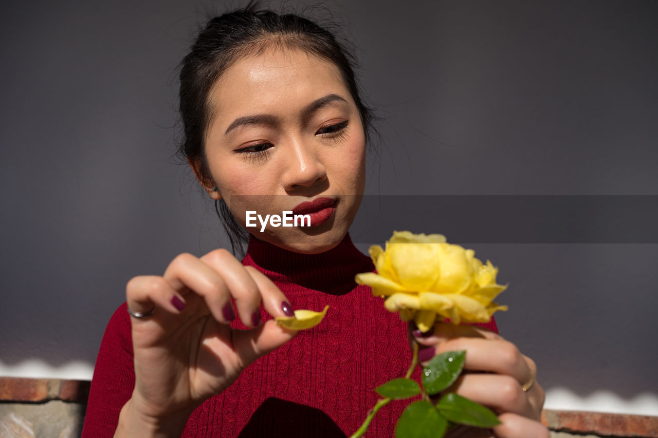 Asian lady tearing petal off yellow rose