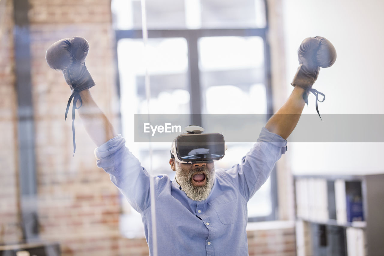 Portrait of businessman with virtual reality glasses and boxing gloves in the office
