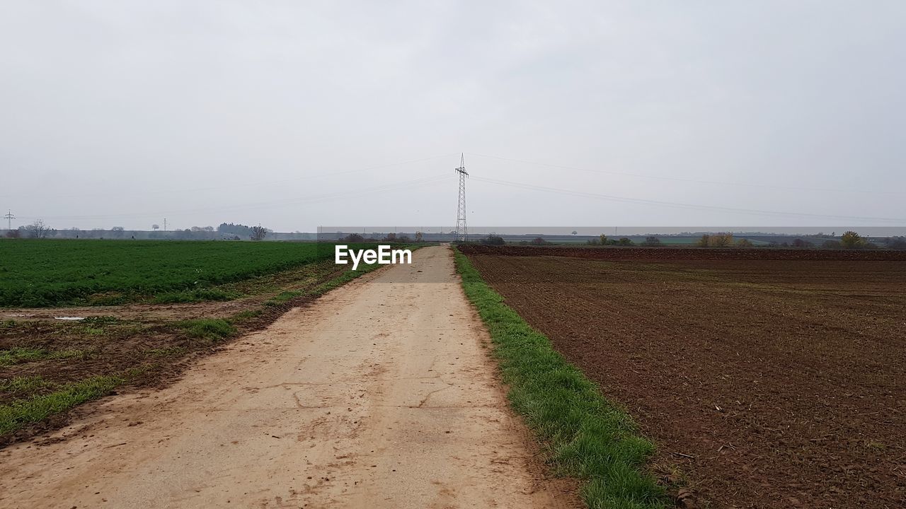 Road passing through agricultural field against sky