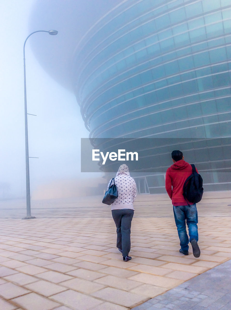 Full length rear view of man and woman walking against building during foggy weather