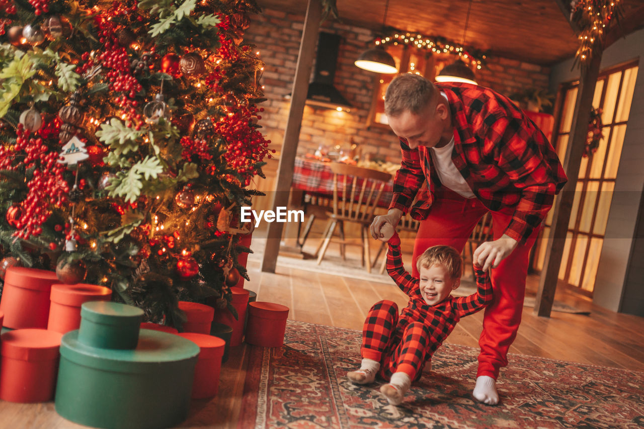 Candid authentic happy dad and son in red plaid pajamas fooling around at wood lodge xmas decorated