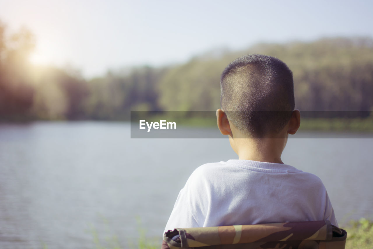 REAR VIEW OF A BOY LOOKING AT LAKE